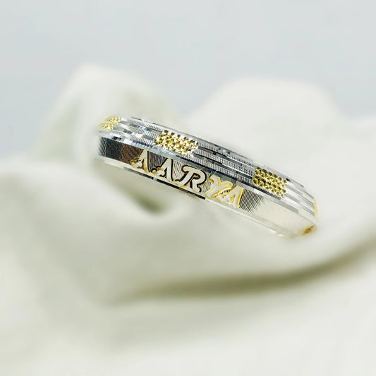 Close-up of silver and gold ring with textured details and engraved name 'ARYA'