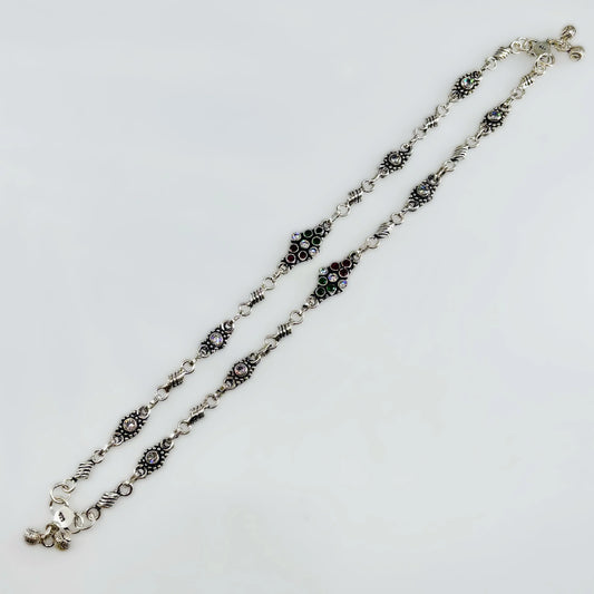 Decorative silver chain necklace with black, green, red, and clear gemstone accents on white background