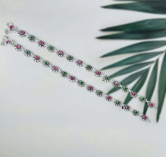 Silver anklets with alternating pink and green round stones on white surface with green leaf