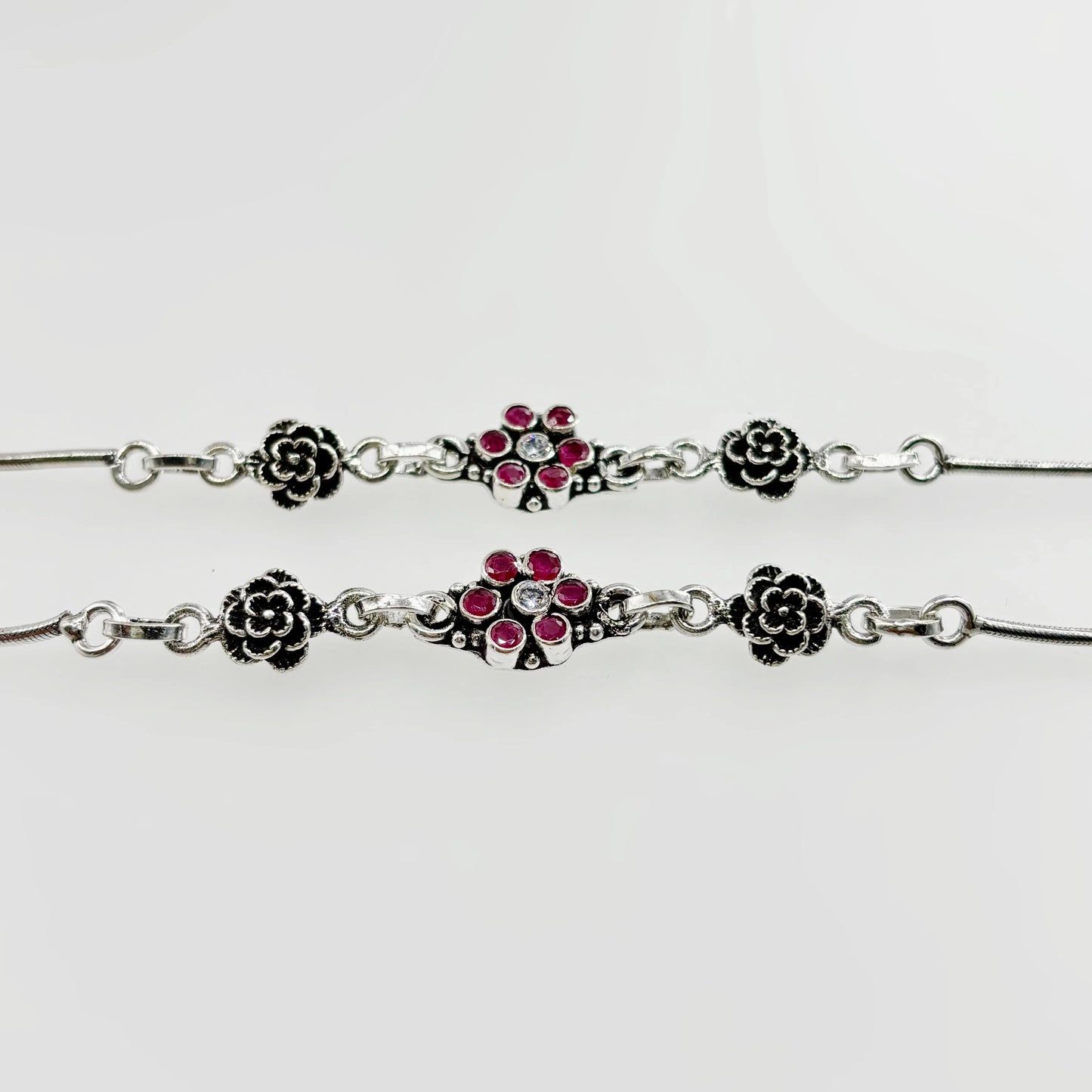 Silver anklets with floral design featuring red and clear gemstones on white background