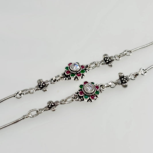 Pair of silver anklets with floral design featuring green and red stones and central clear crystals