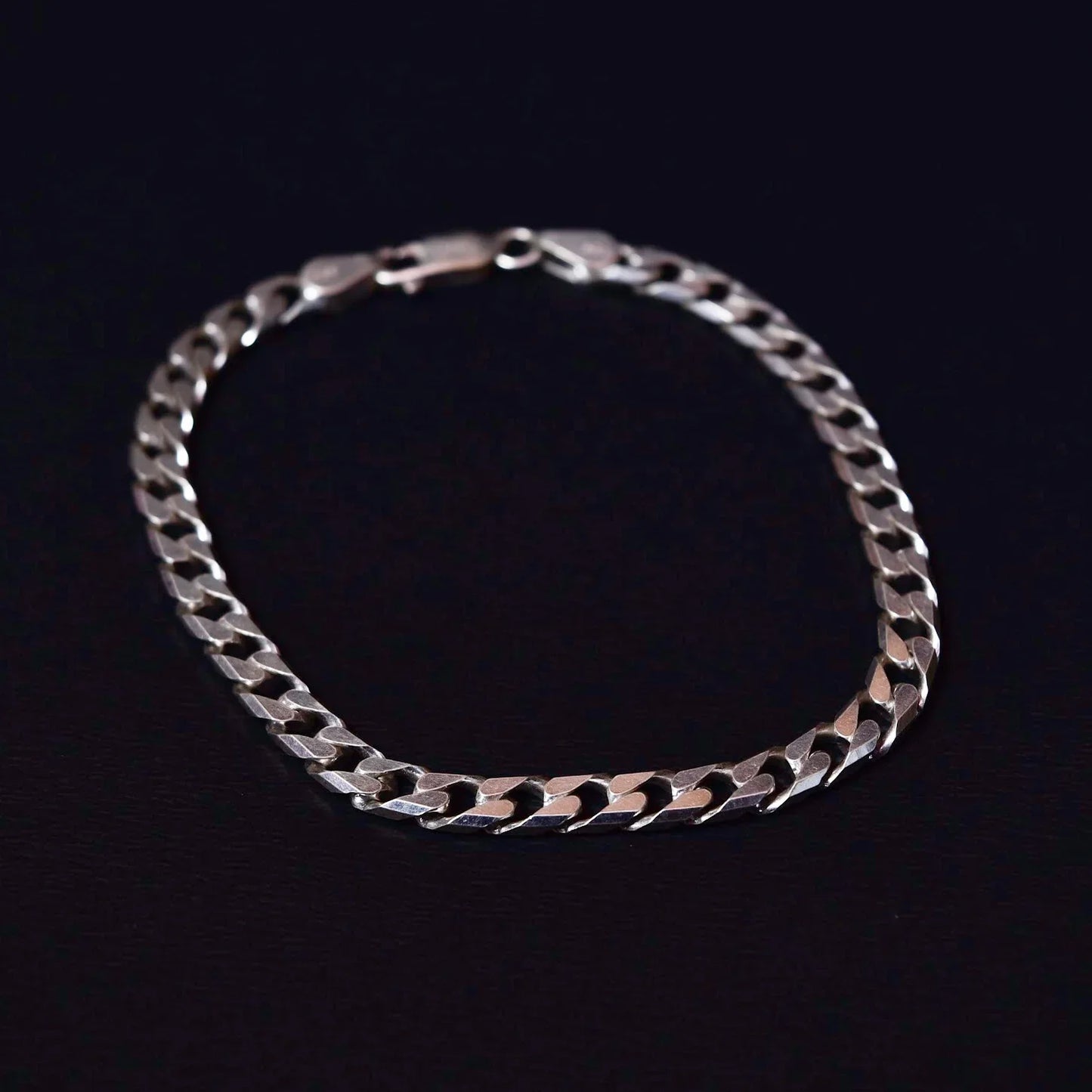 Silver flat curb chain bracelet with lobster clasp on black background