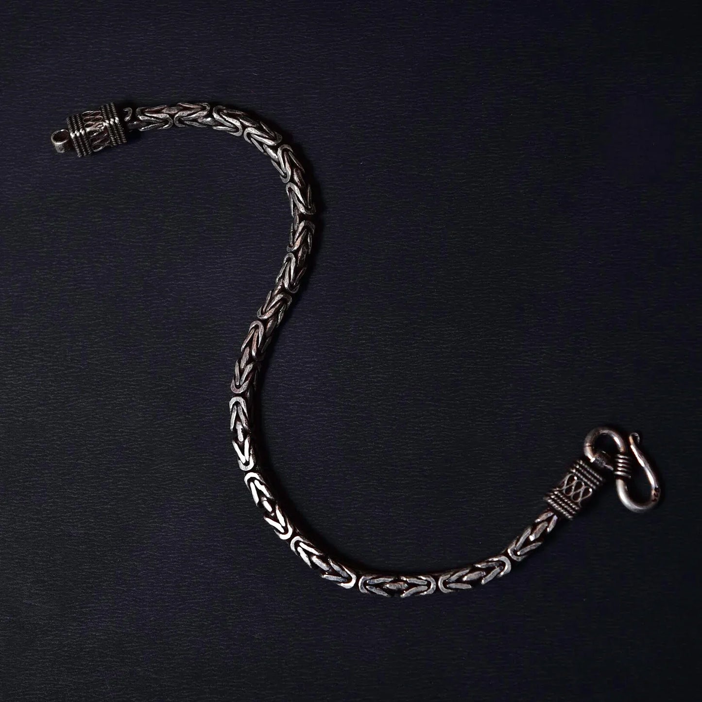 Elegant silver chain bracelet with intricate woven link design on black background