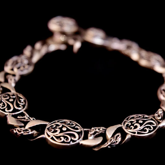 Close-up of ornate silver bracelet with intricate filigree round links on black background