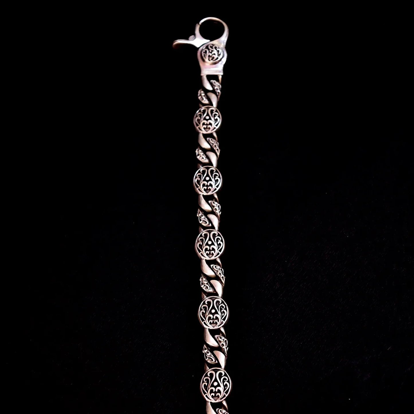 Silver bracelet with intricate round filigree designs and a lobster clasp on black background