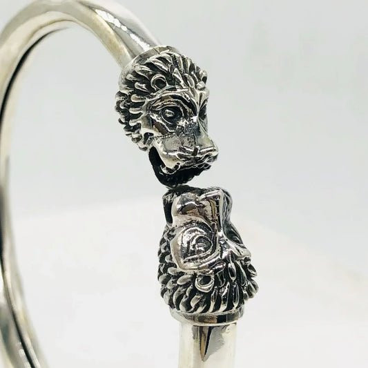 Close-up of a silver bracelet with detailed lion head designs on each end against a plain white background