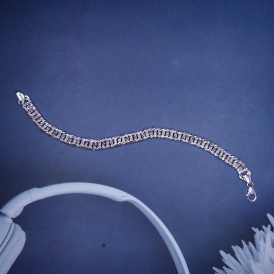Silver chain bracelet with clasp on dark blue background near white headphones and flower