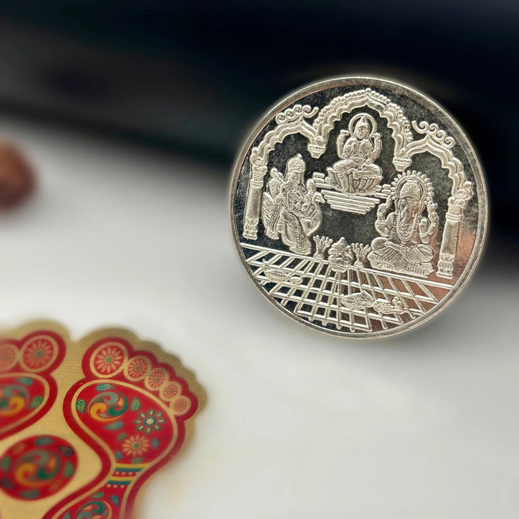 Silver coin with engraved Hindu deities and ornate arch, next to decorative colorful footprints