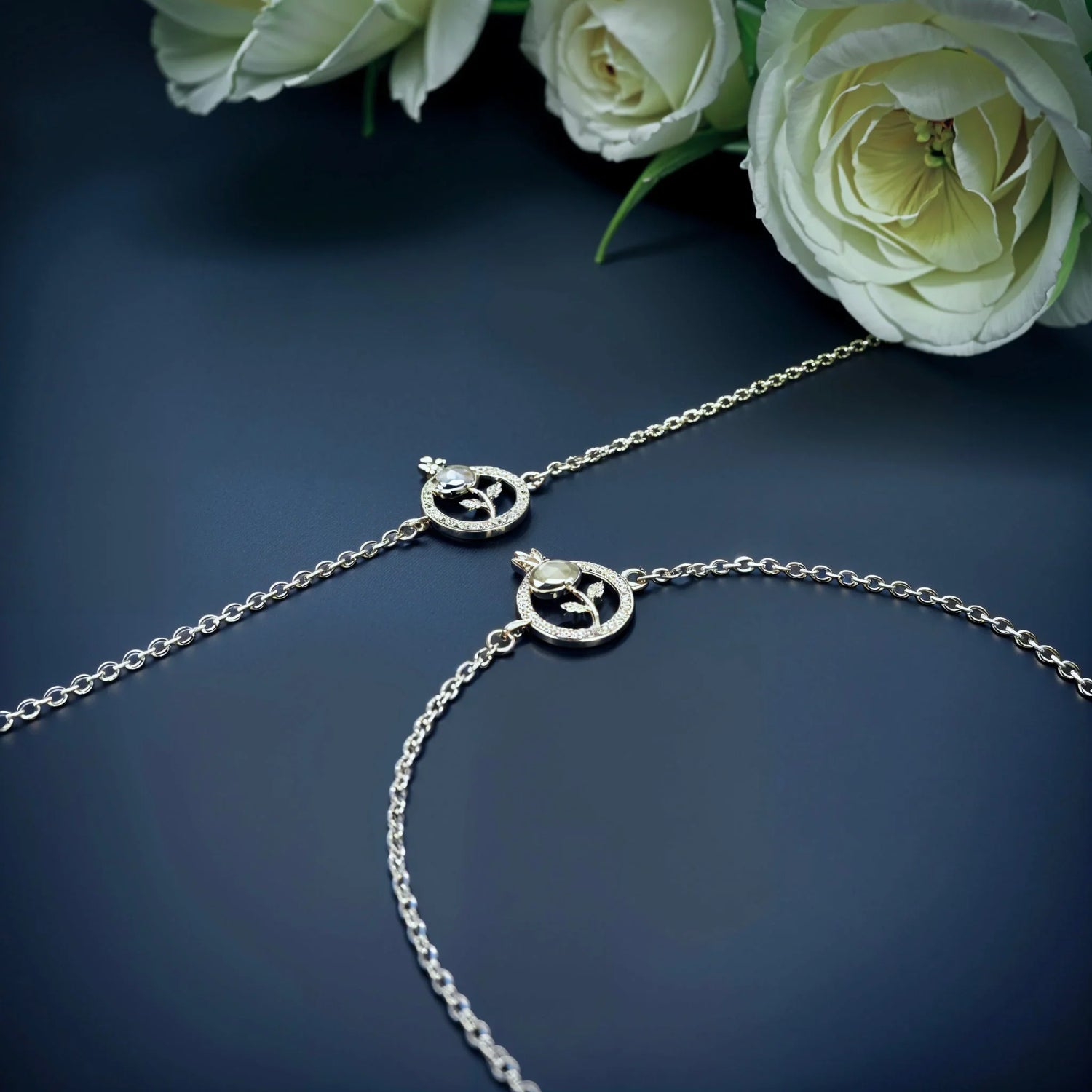 Silver bracelets with circular floral charms and clear stones on dark surface with white roses