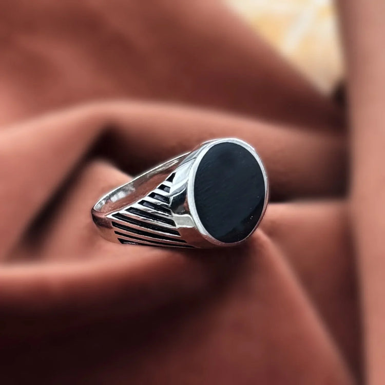 Silver ring with round black stone and striped band on brown fabric background