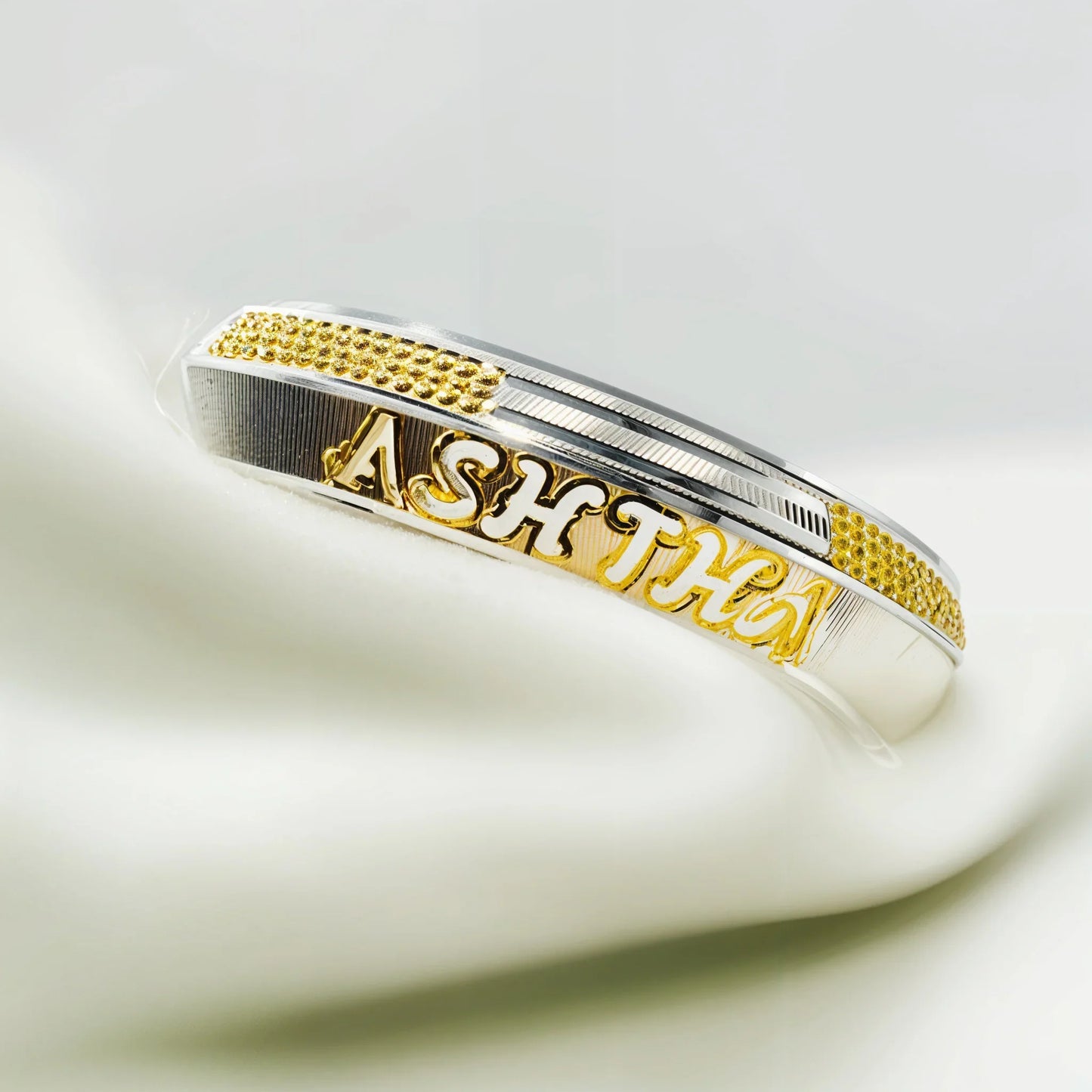 Silver and gold personalized bracelet with the name ASHTHA on white fabric background