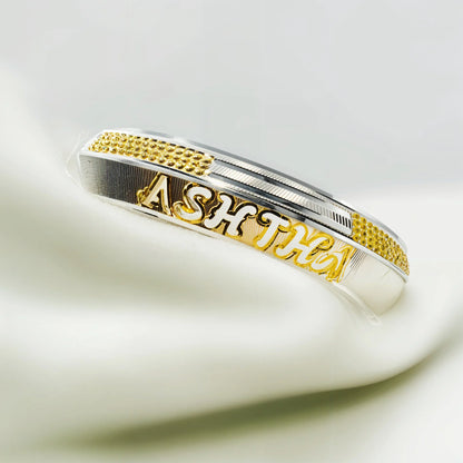Silver and gold personalized bracelet with the name ASHTHA on white fabric background