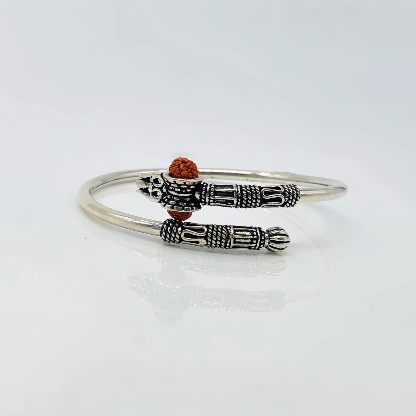 Intricate silver bracelet with detailed tribal pattern and small brown bead accent on white surface