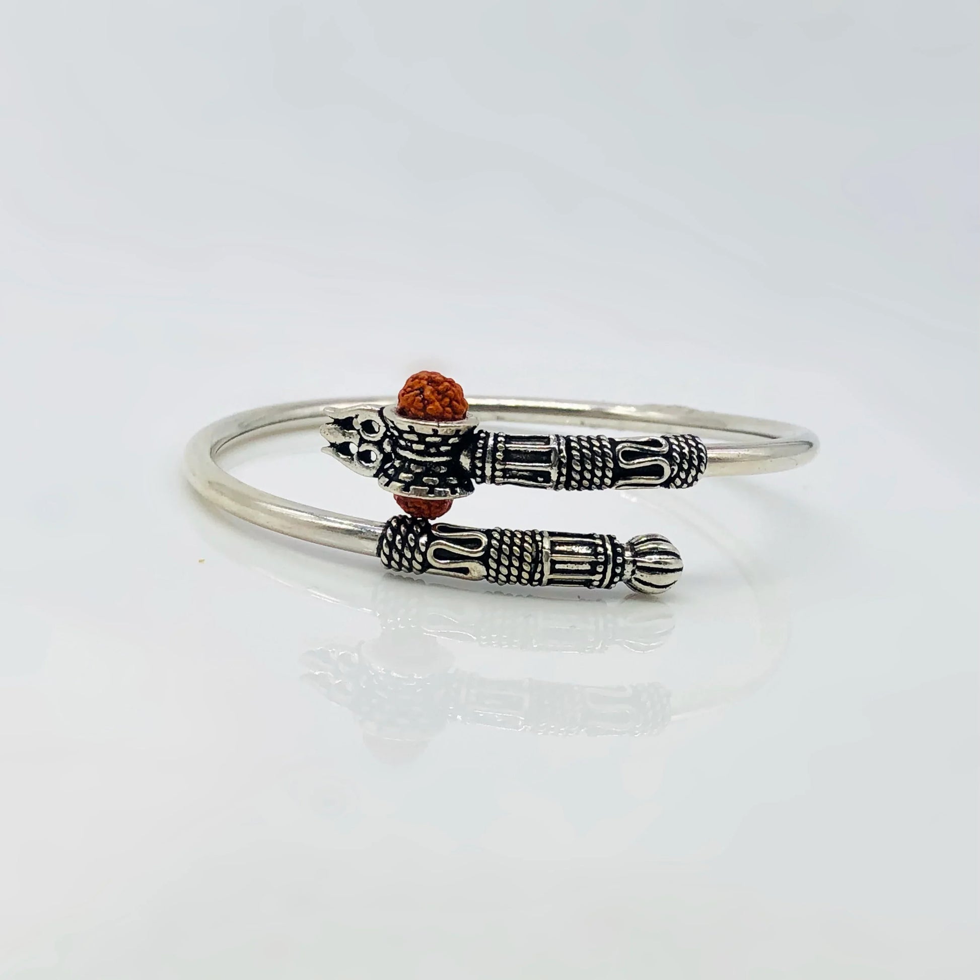 Intricate silver bracelet with detailed tribal pattern and small brown bead accent on white surface