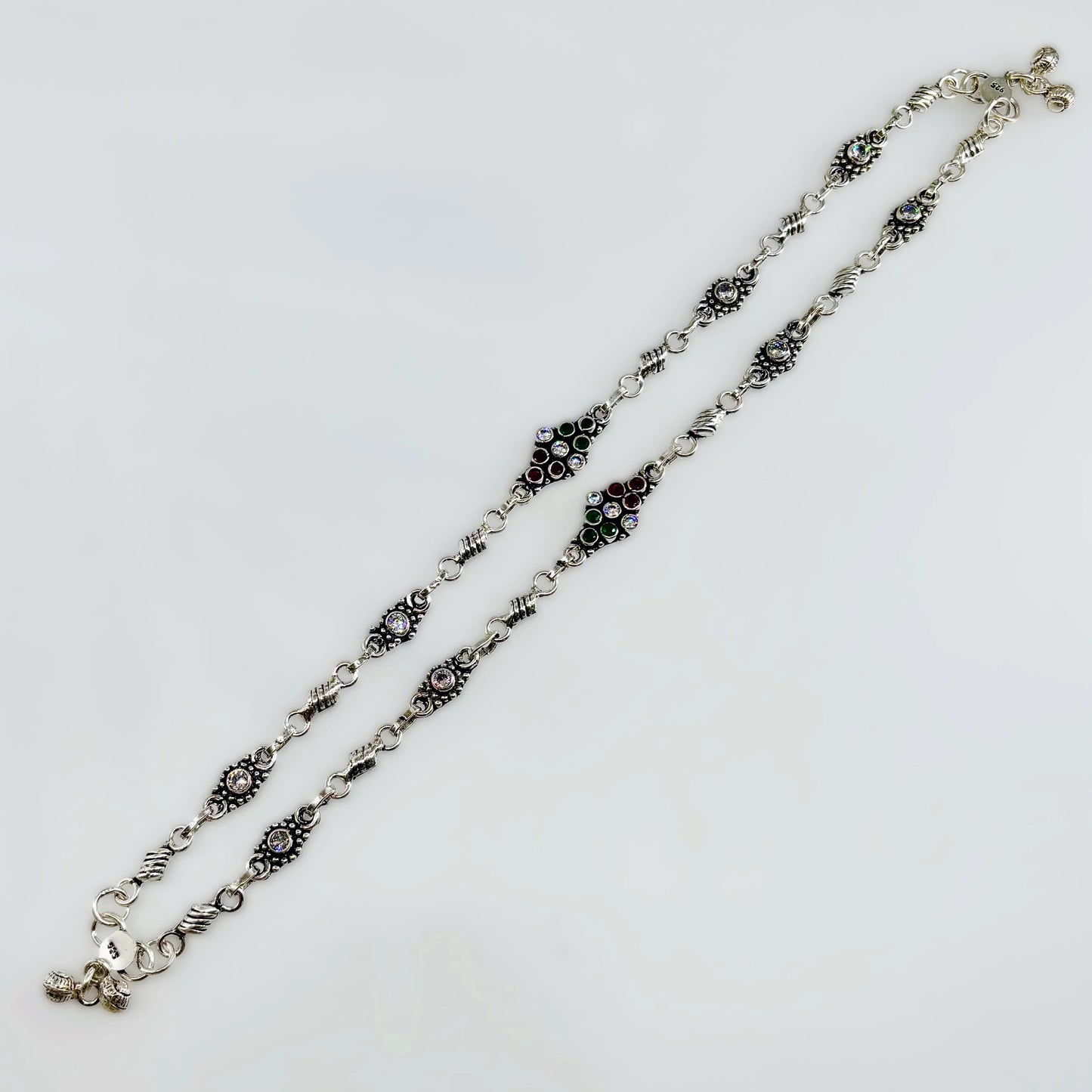 Decorative silver chain necklace with black, green, red, and clear gemstone accents on white background