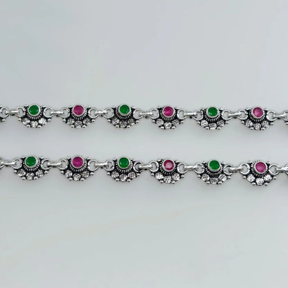 Silver anklets with alternating green and pink stones in decorative settings on white background