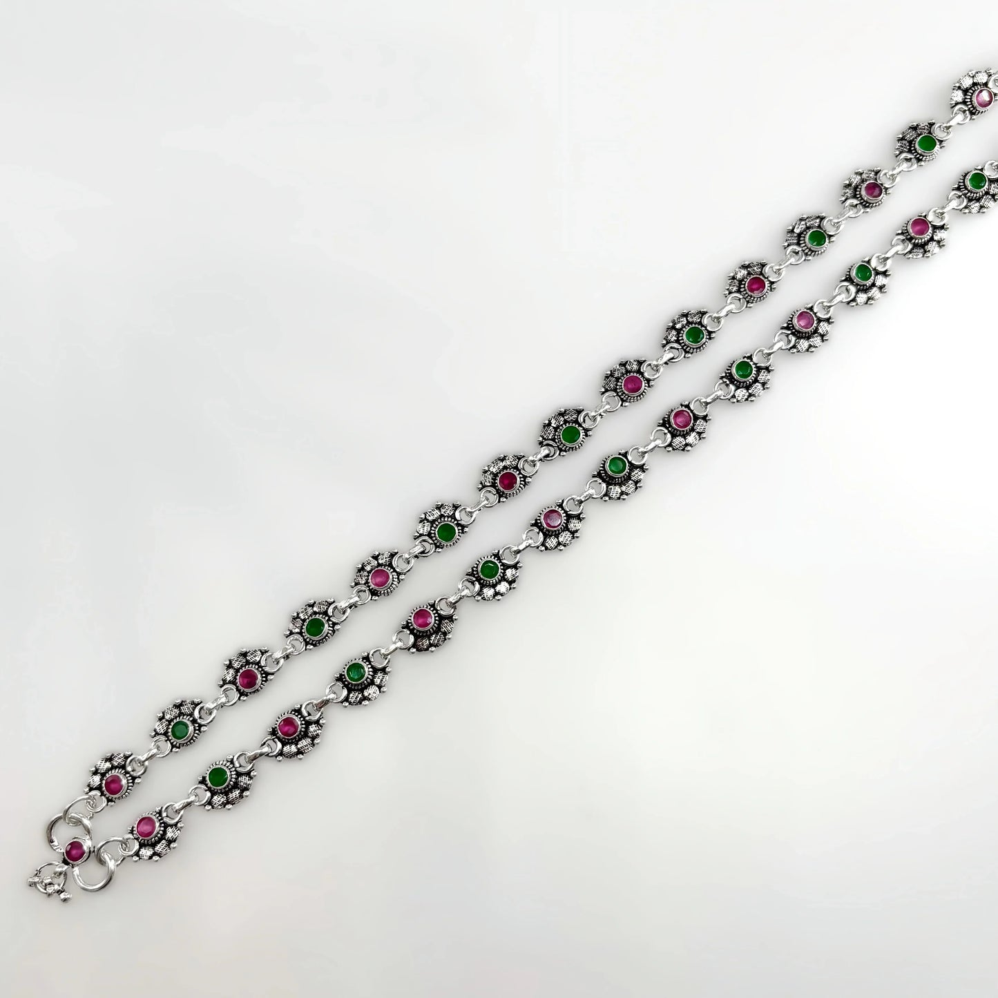 Silver anklets with alternating pink and green stones in floral settings on white background