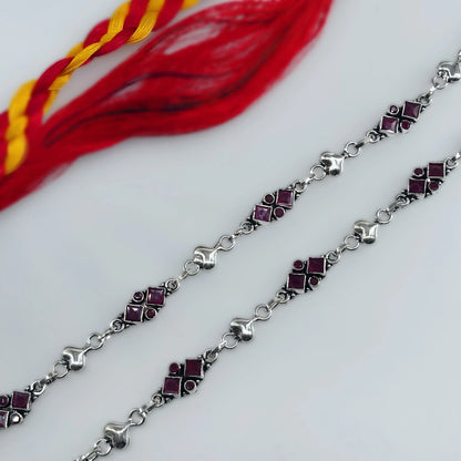 Traditional silver anklet with red stones and red-yellow braided thread on white background