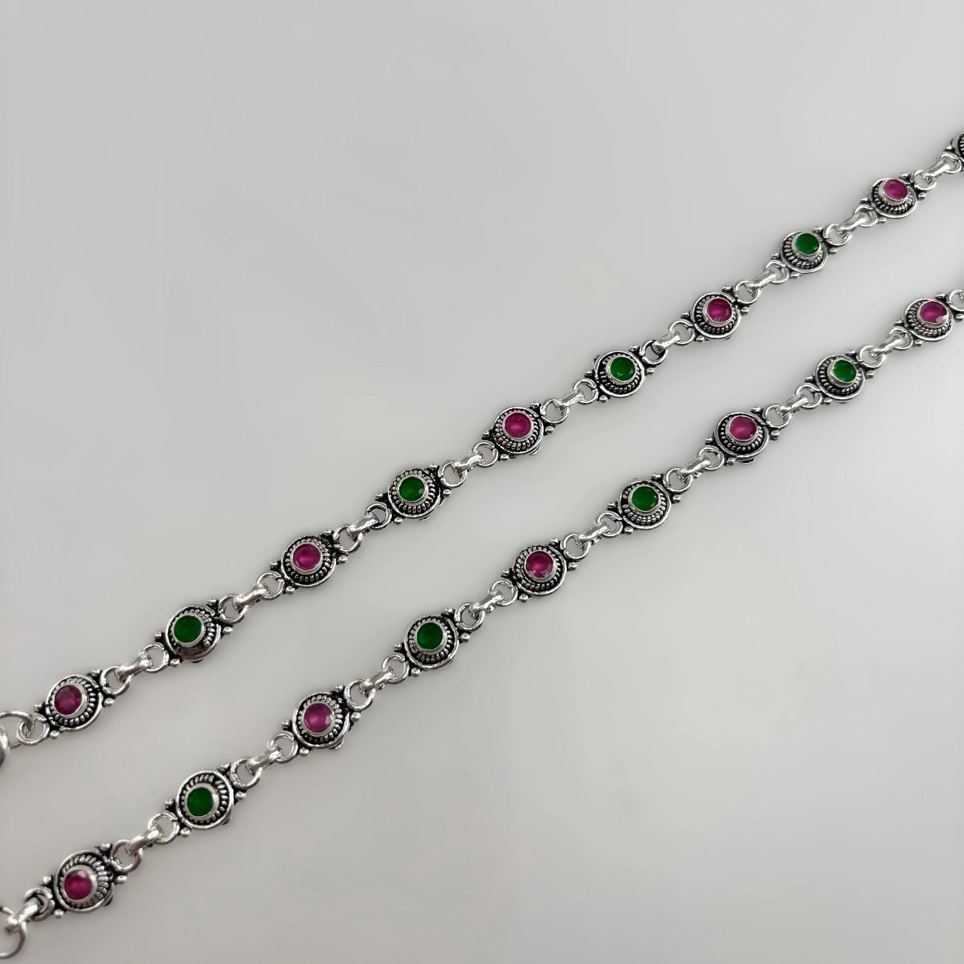 Silver chain anklets with alternating pink and green round stones on white background