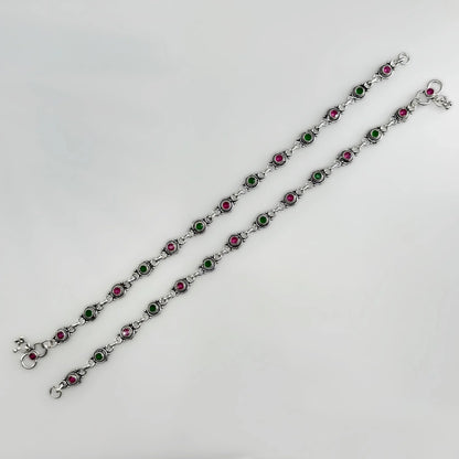 Two silver anklets with alternating green and pink stone settings on a white background