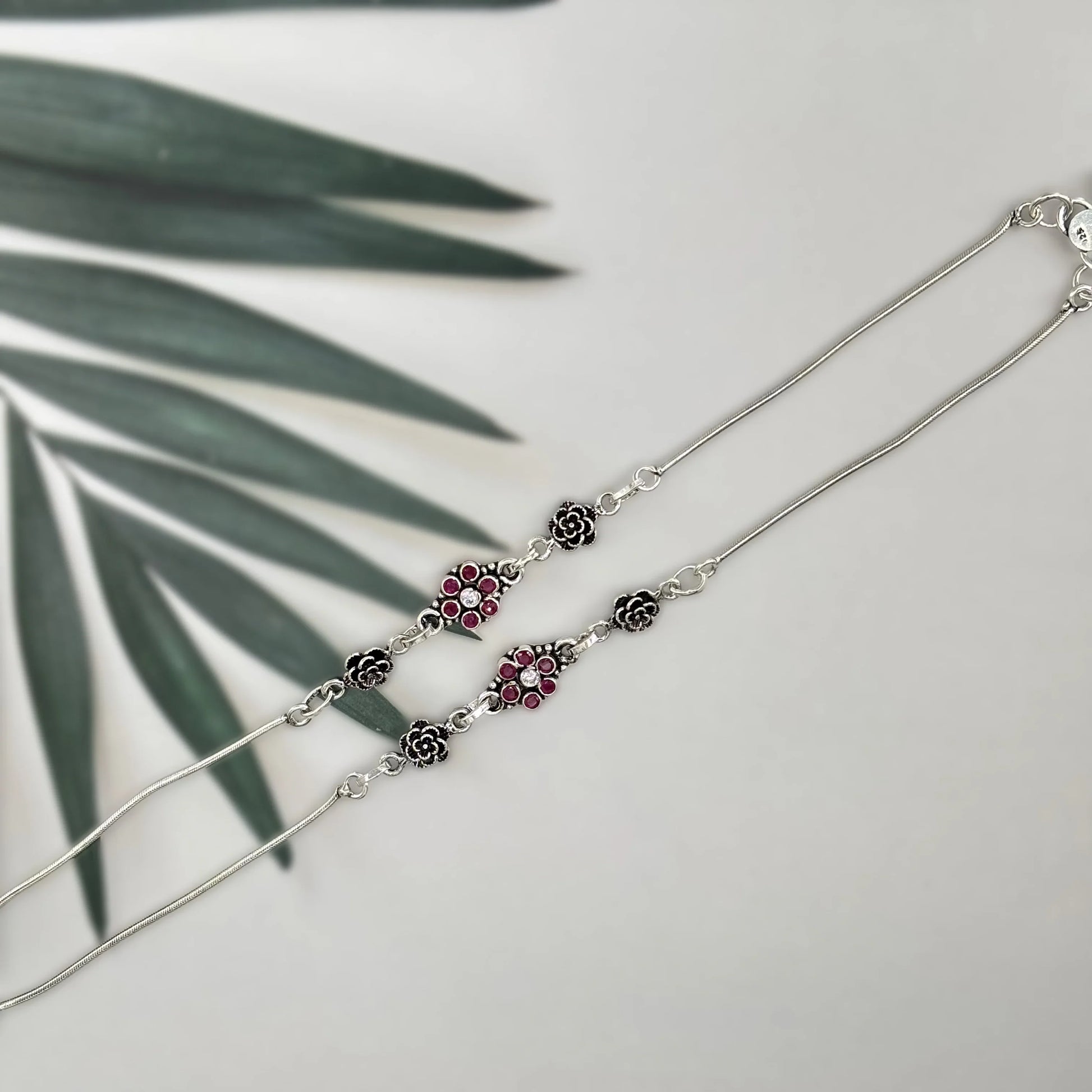 Silver necklace with floral and ruby gemstone accents on a white background with green leaf