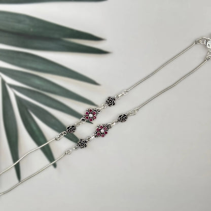 Silver necklace with floral and ruby gemstone accents on a white background with green leaf