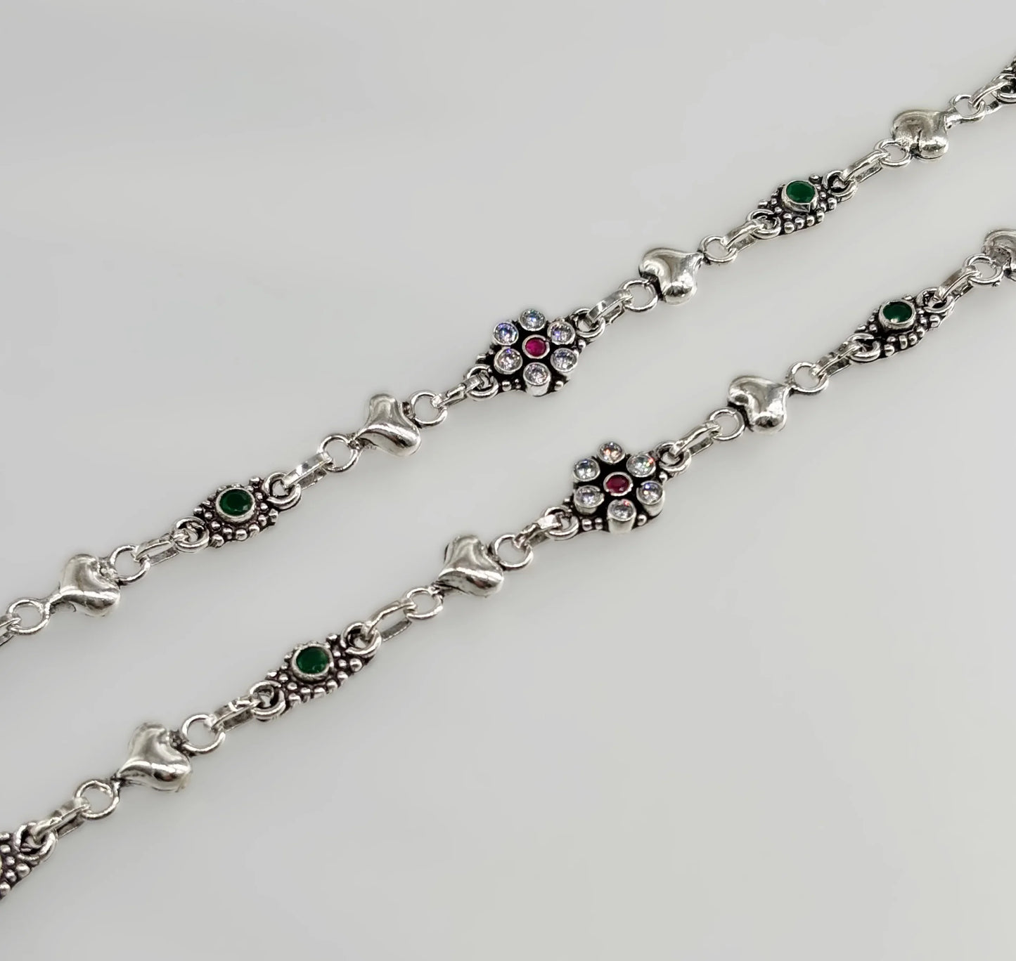 close-up of silver bracelet with green and red stones and embedded clear crystals on white background