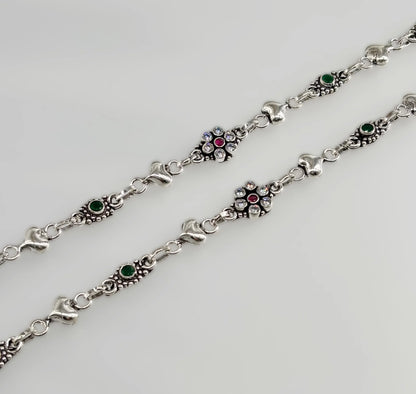 close-up of silver bracelet with green and red stones and embedded clear crystals on white background