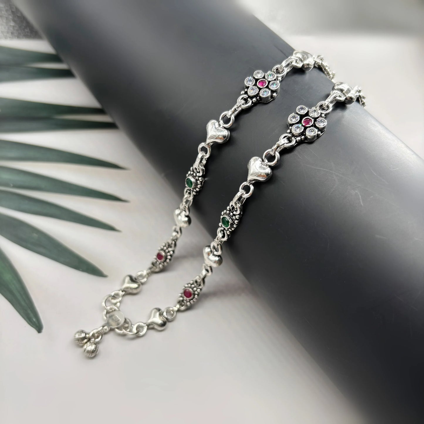Silver anklet with heart charms and multicolored gemstones on black display against white background