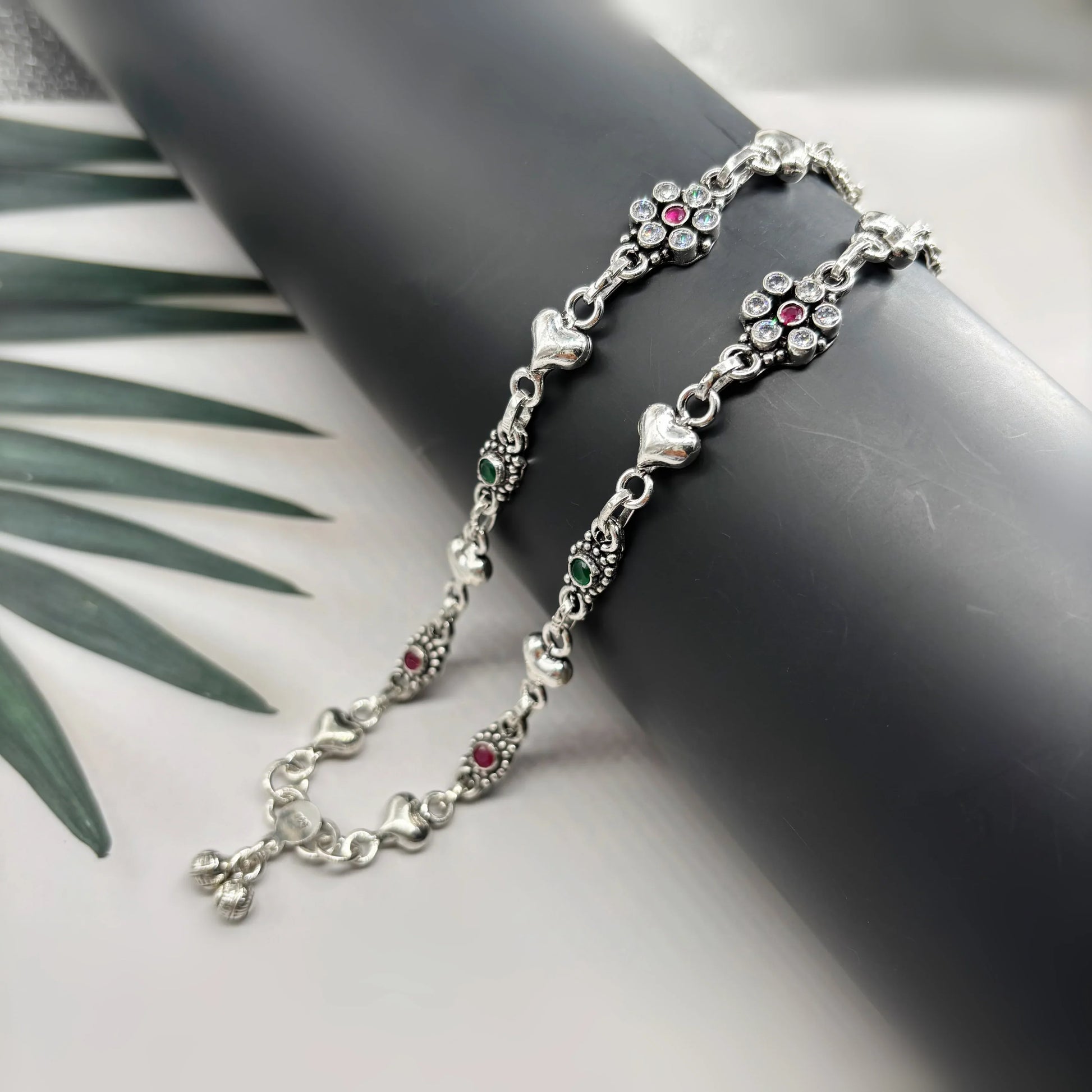 Silver anklet with heart charms and multicolored gemstones on black display against white background