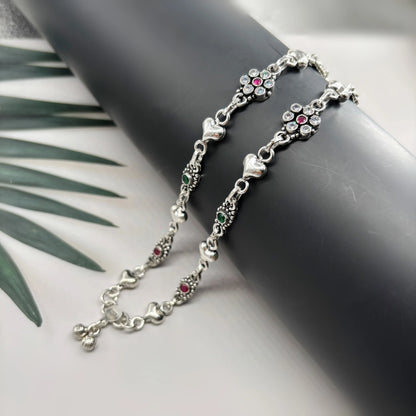 Silver anklet with heart charms and multicolored gemstones on black display against white background
