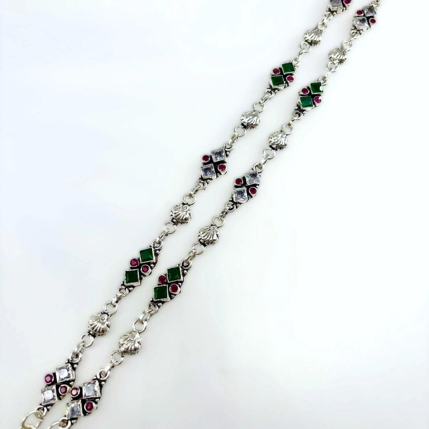 Silver chain necklace with green, red, and clear square gemstones on white background