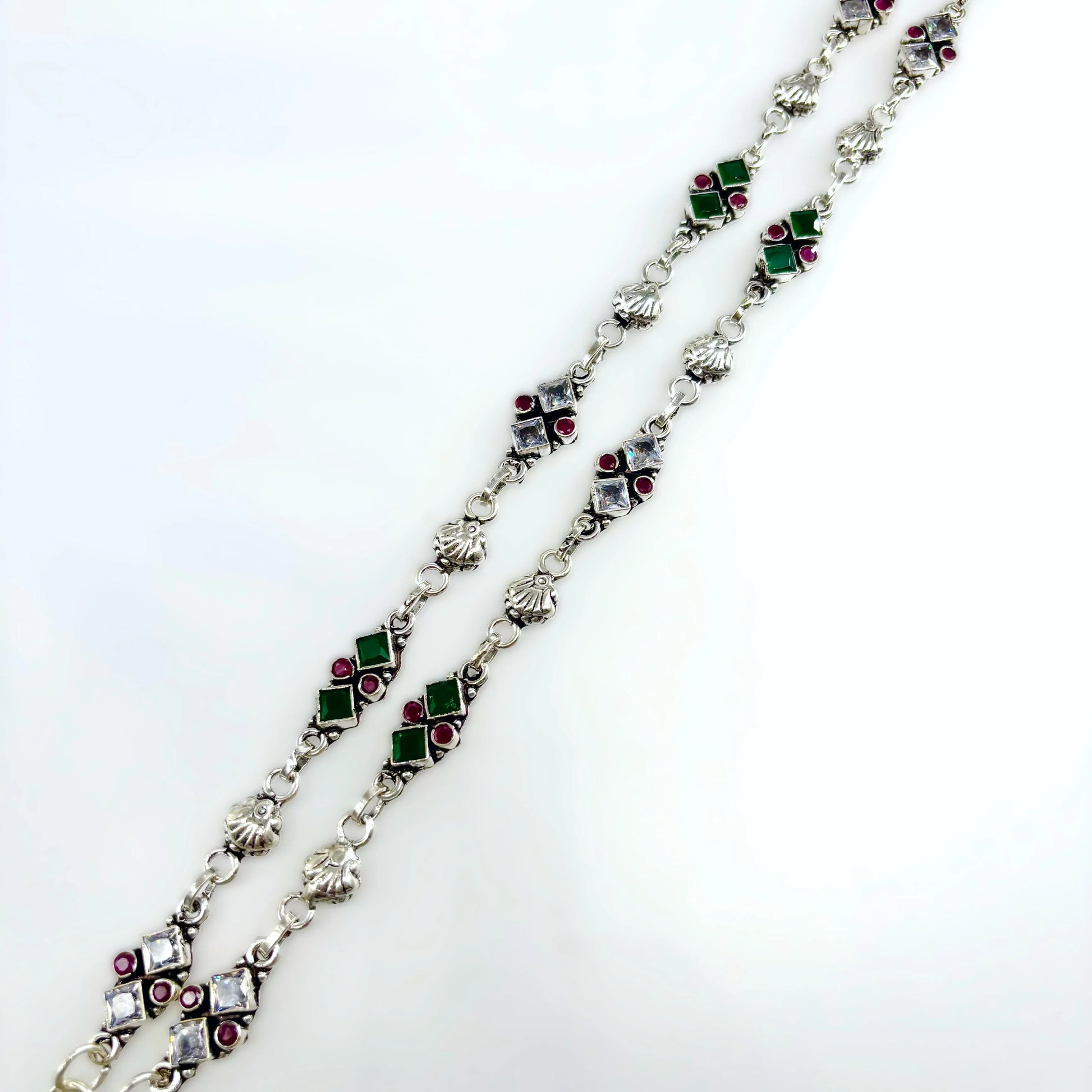 Silver chain necklace with green, red, and clear square gemstones on white background