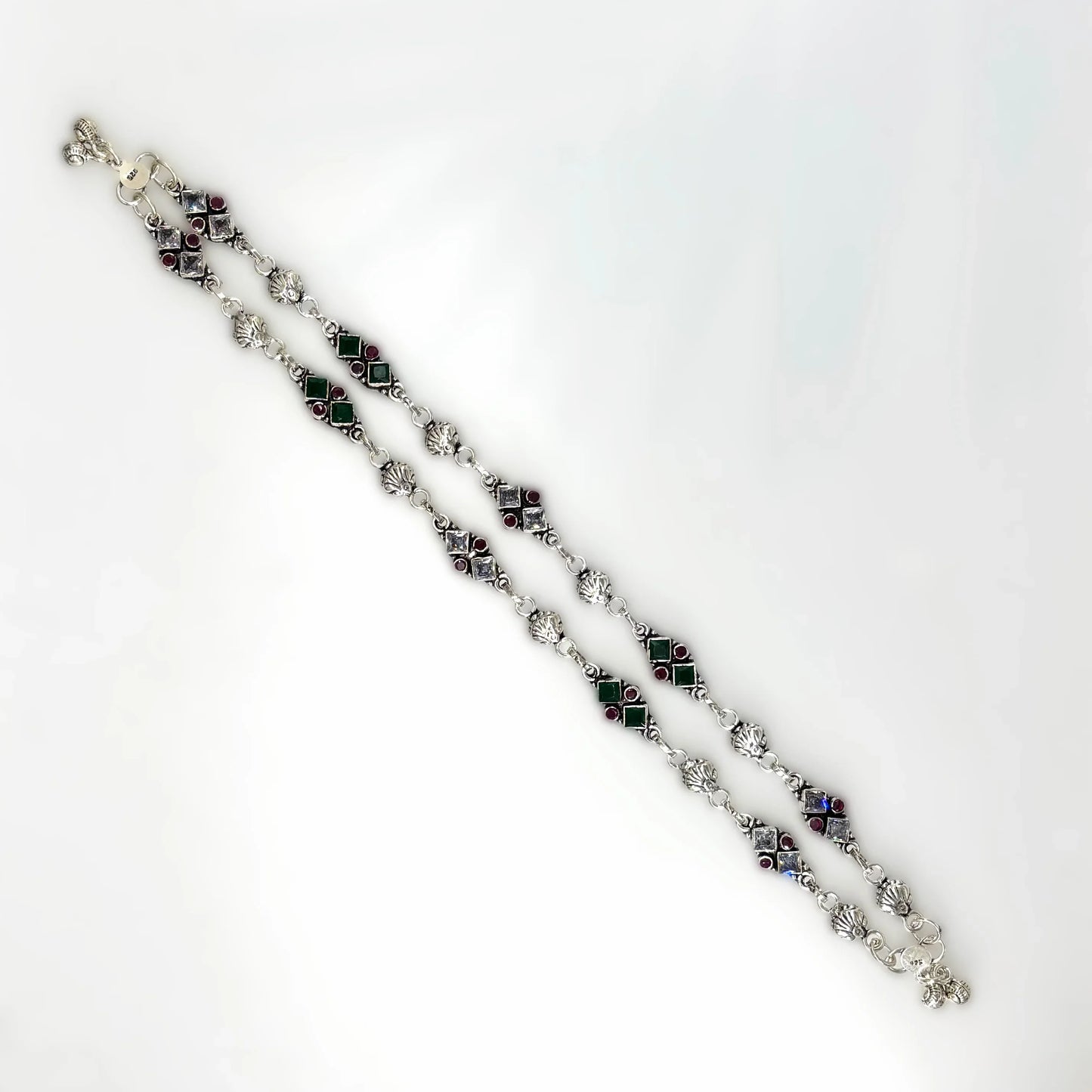 Silver anklets with red and green square gemstones and intricate links on white background