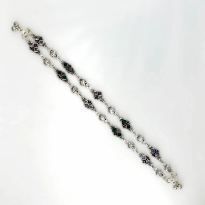 Silver anklets with red and green square gemstones and intricate links on white background