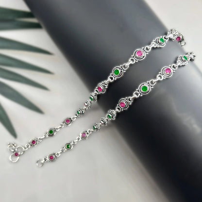 Silver chain anklets with alternating green and pink round stones on black surface