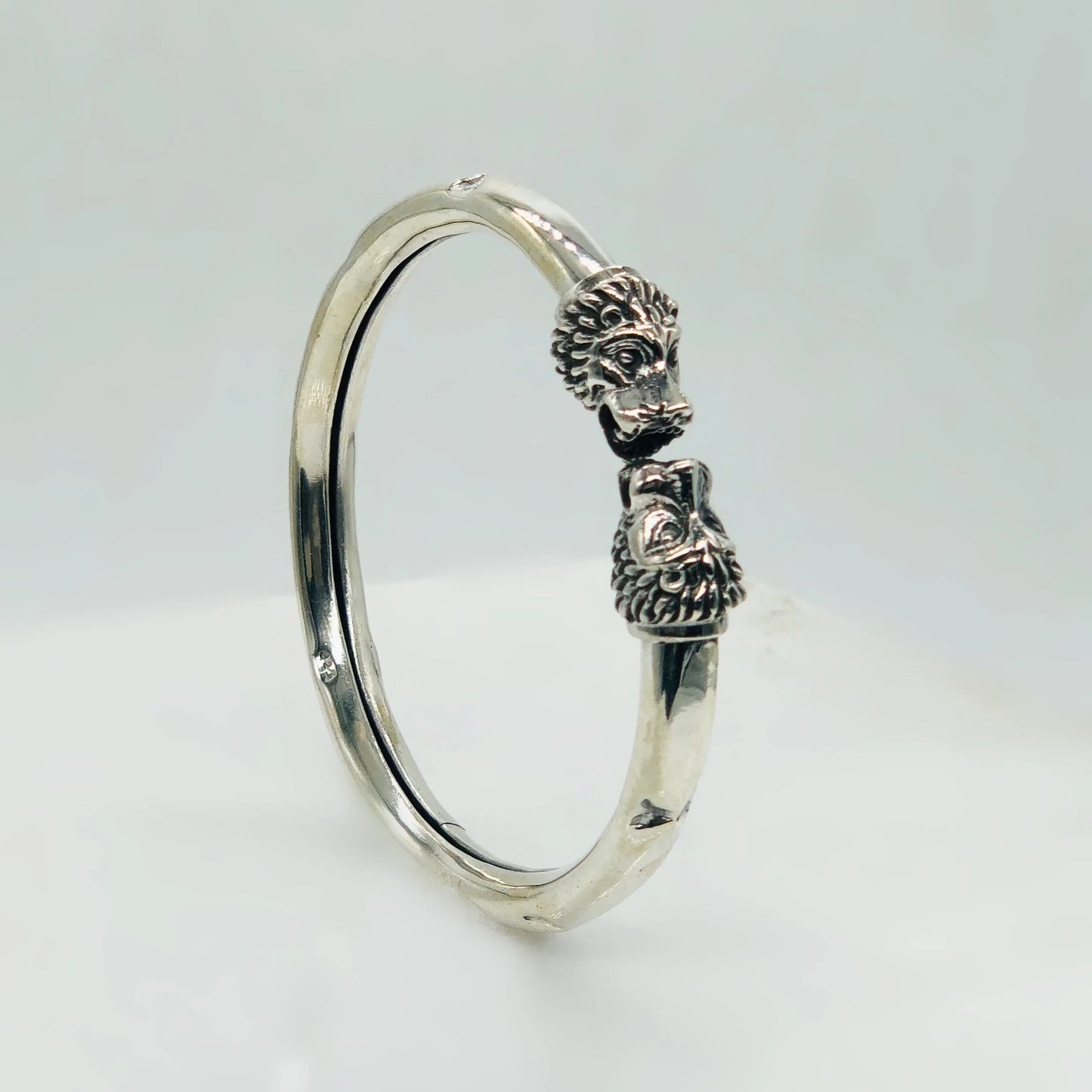 Silver bracelet with detailed lion head designs on both ends against a white background
