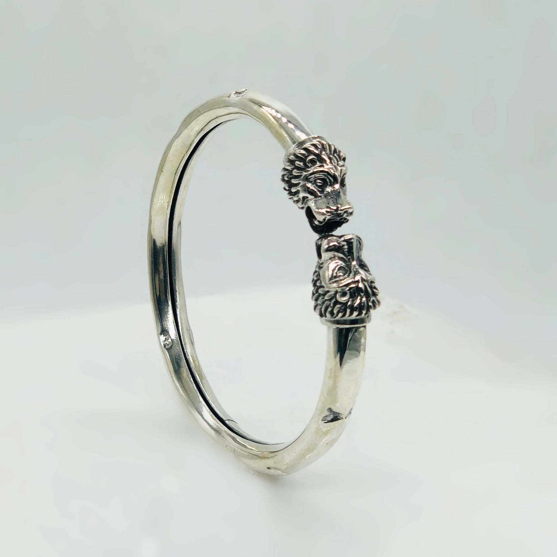 Silver bracelet with detailed lion head designs on both ends against a white background