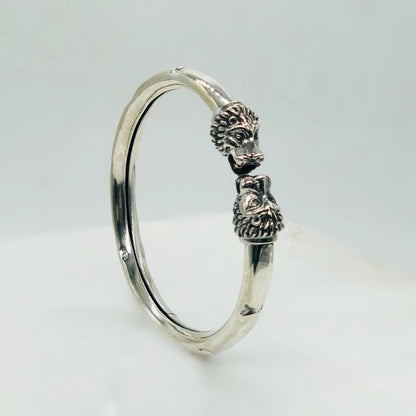 Silver bracelet with detailed lion head designs on both ends against a white background