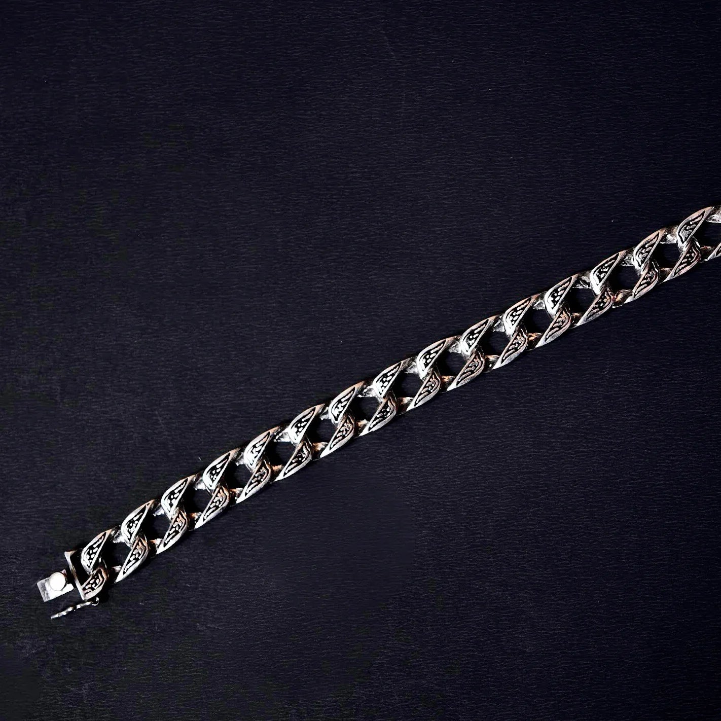 Silver Cuban link chain bracelet with intricate engraved details on black background