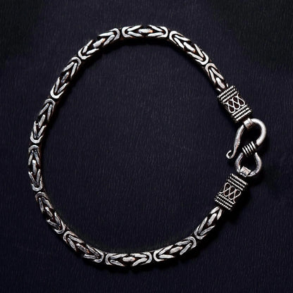 Silver chain bracelet with intricate woven pattern and decorative clasp on black background
