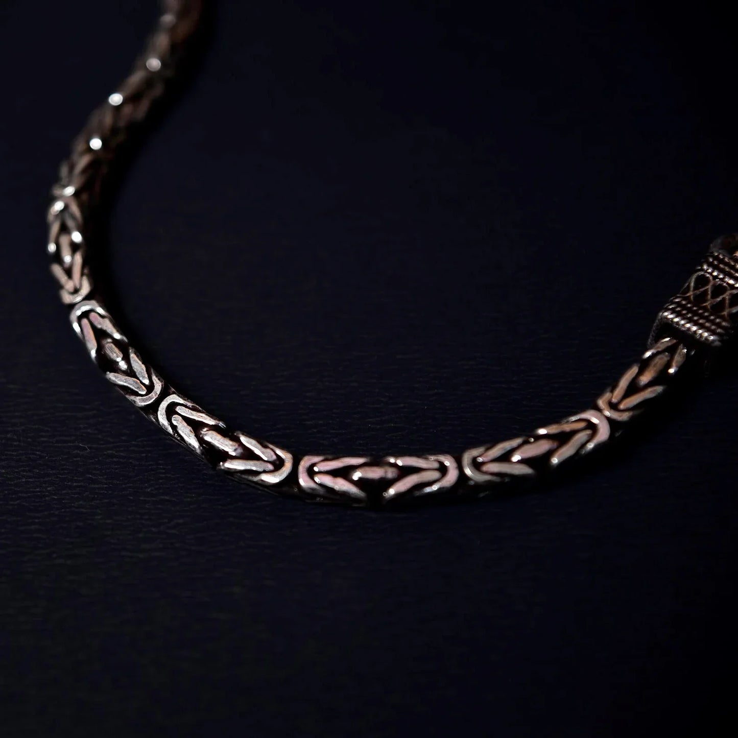 Close-up of a silver bracelet with intricate geometric and braided patterns on a dark background