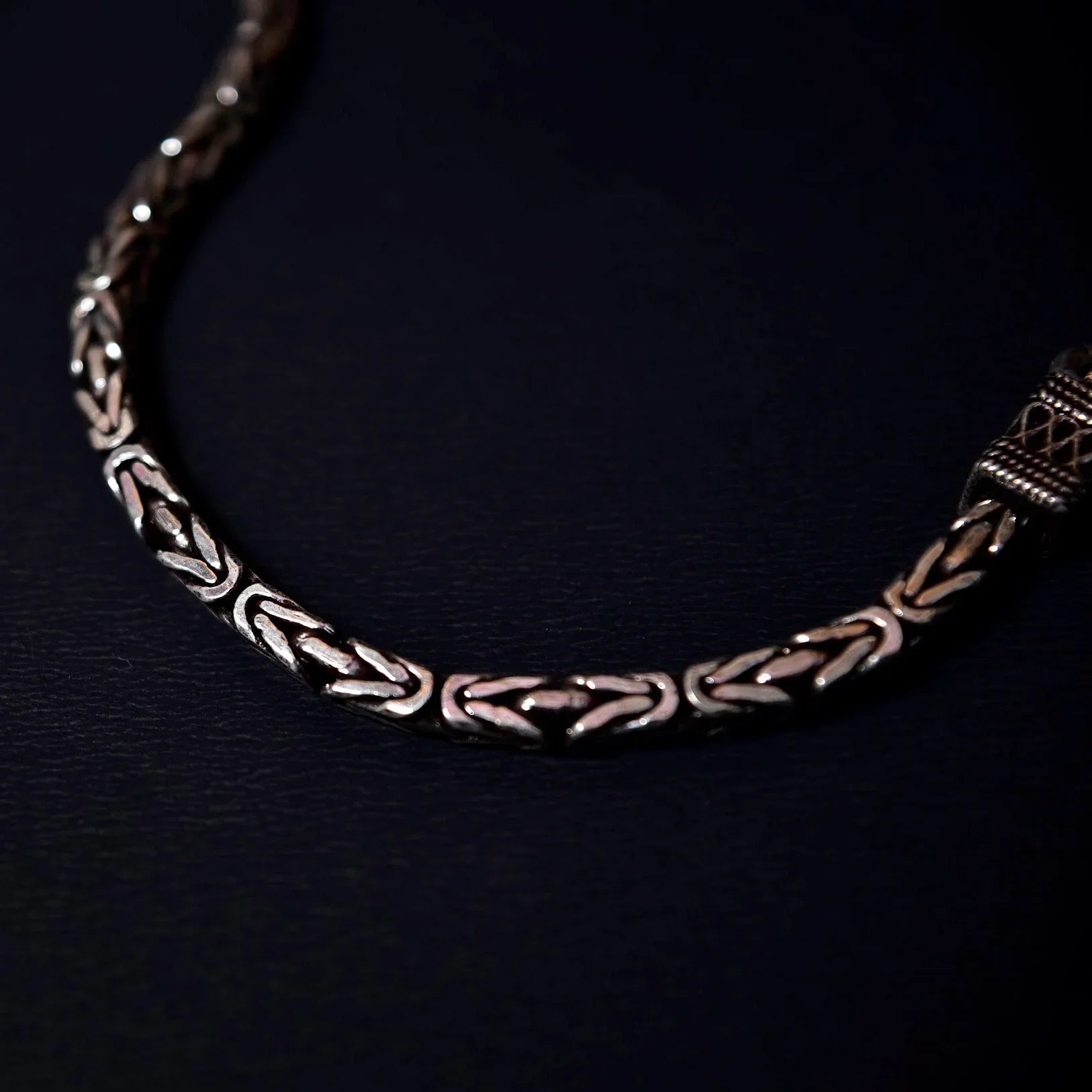Close-up of a silver bracelet with intricate geometric and braided patterns on a dark background