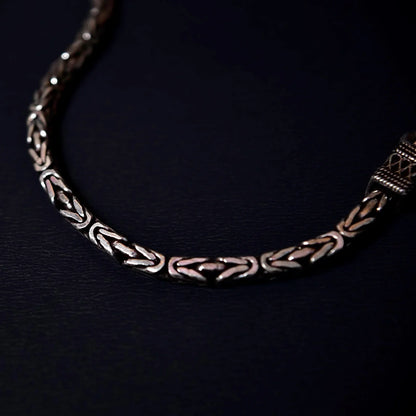 Close-up of a silver bracelet with intricate geometric and braided patterns on a dark background