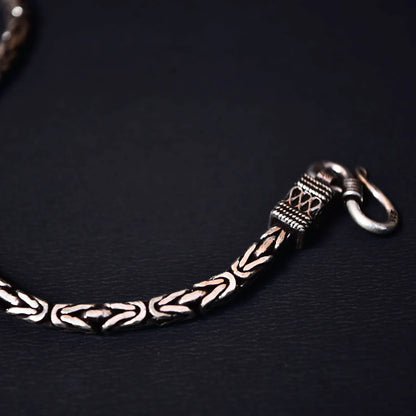 Close-up of a silver chain bracelet with intricate braided links and a hook clasp on a black background