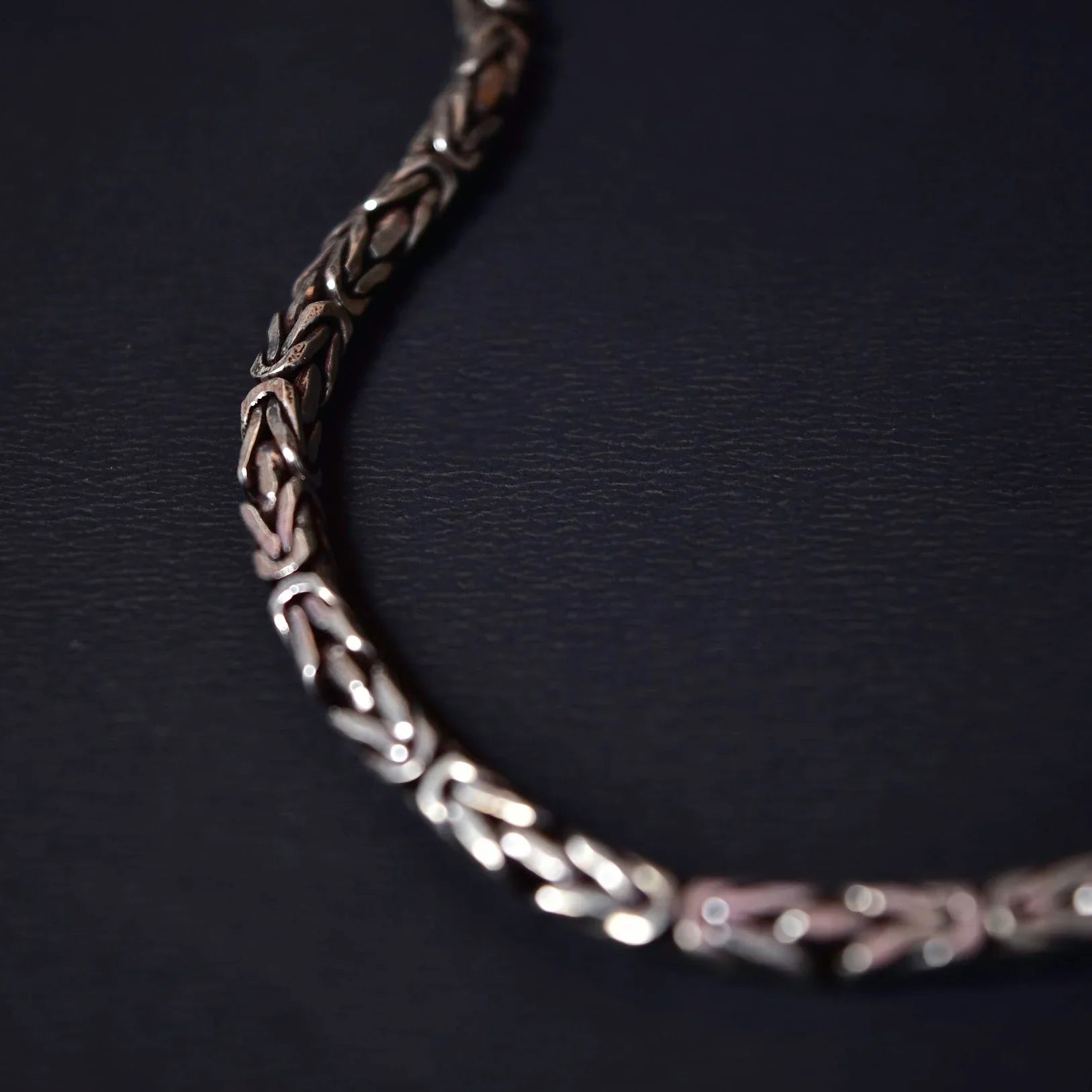 Close-up of silver intricate woven chain bracelet on dark textured surface