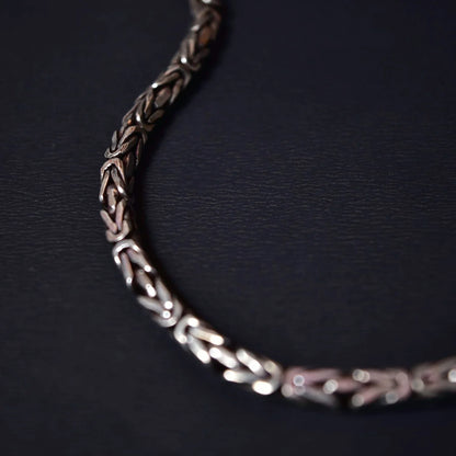 Close-up of silver intricate woven chain bracelet on dark textured surface