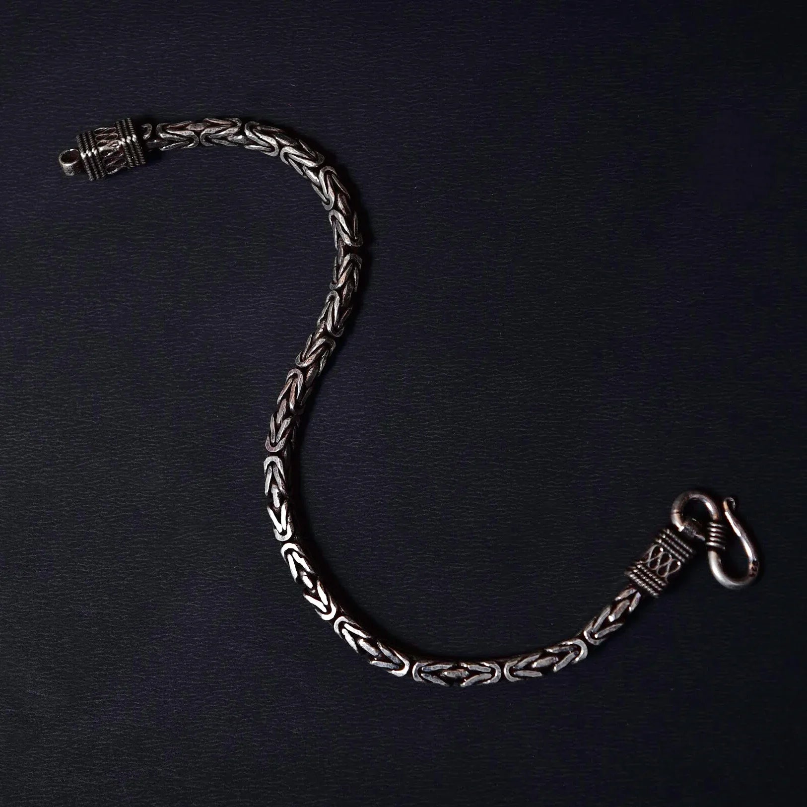 Elegant silver chain bracelet with intricate woven link design on black background