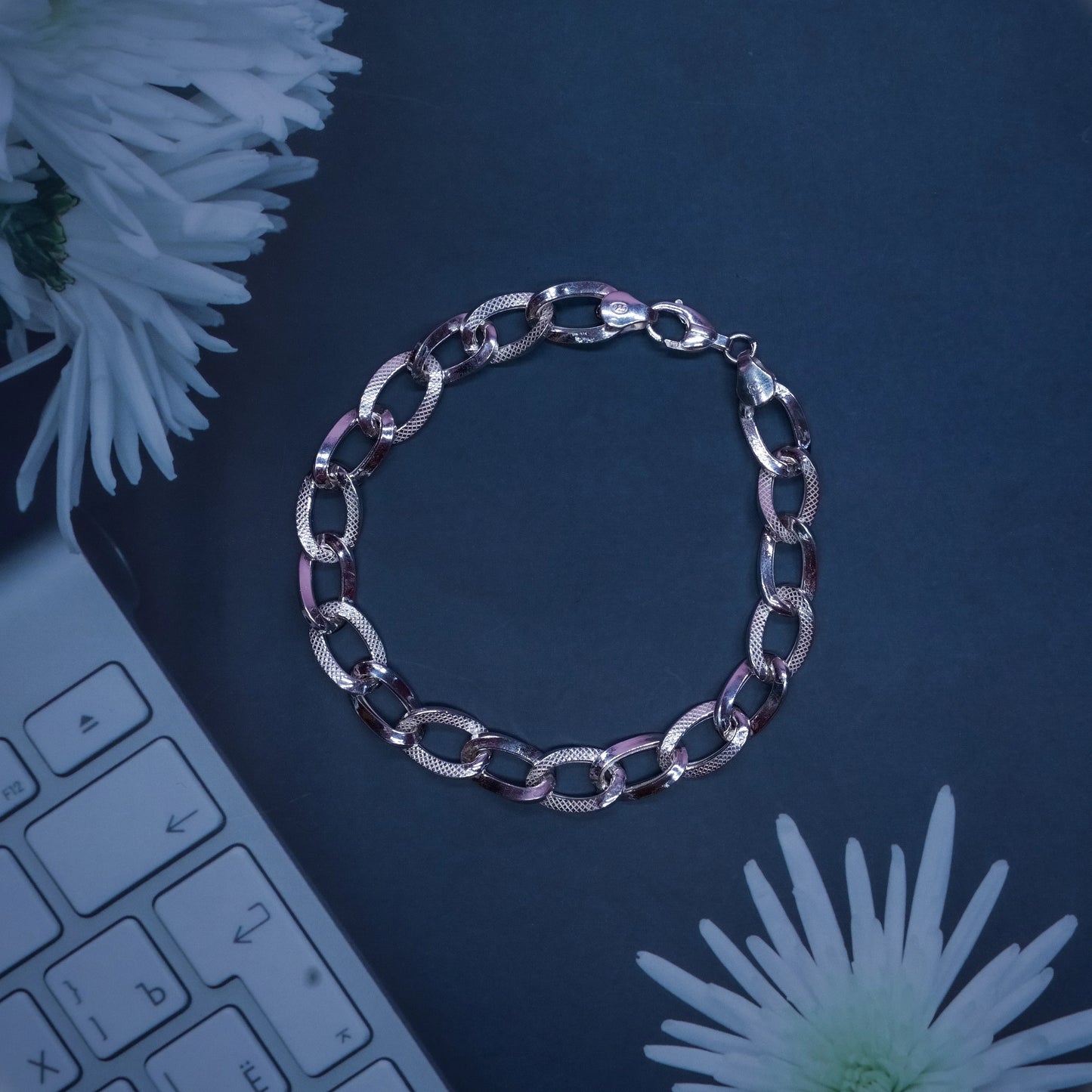 silver chain bracelet on black surface with white flowers and keyboard edge