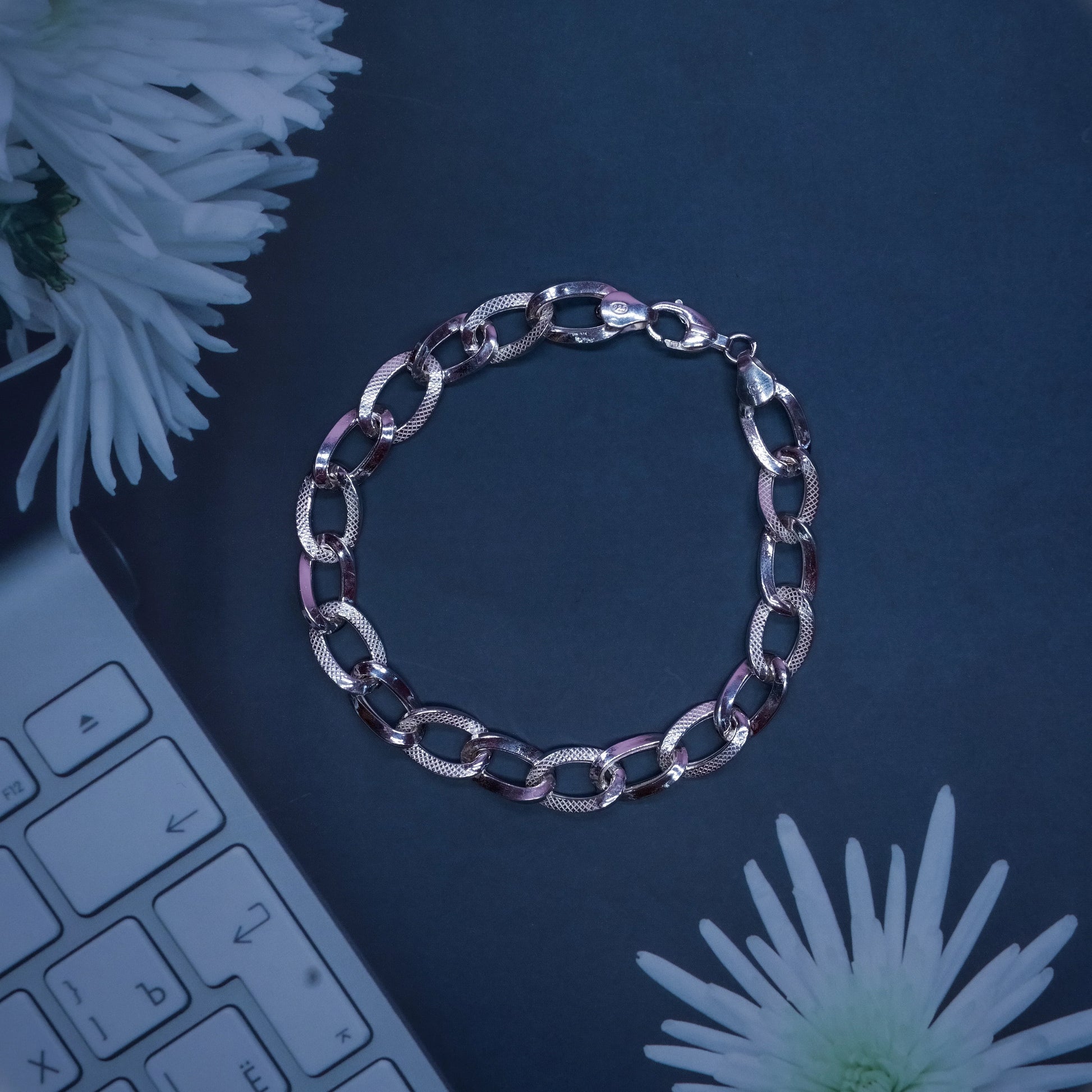 silver chain bracelet on black surface with white flowers and keyboard edge